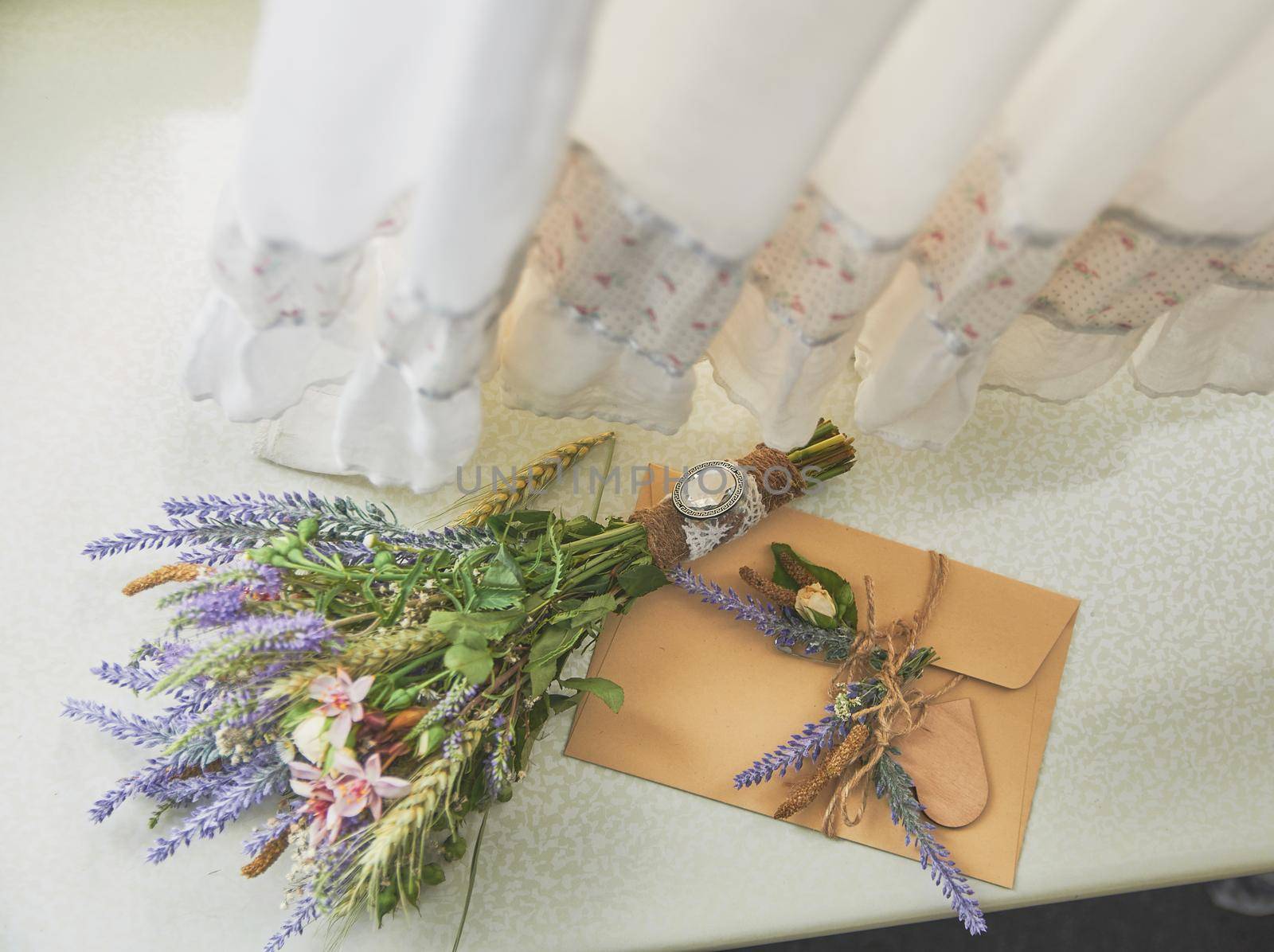 bridal bouquet of lavender in a boho style lies on the window near the handmade envelope, on top of the wedding dress