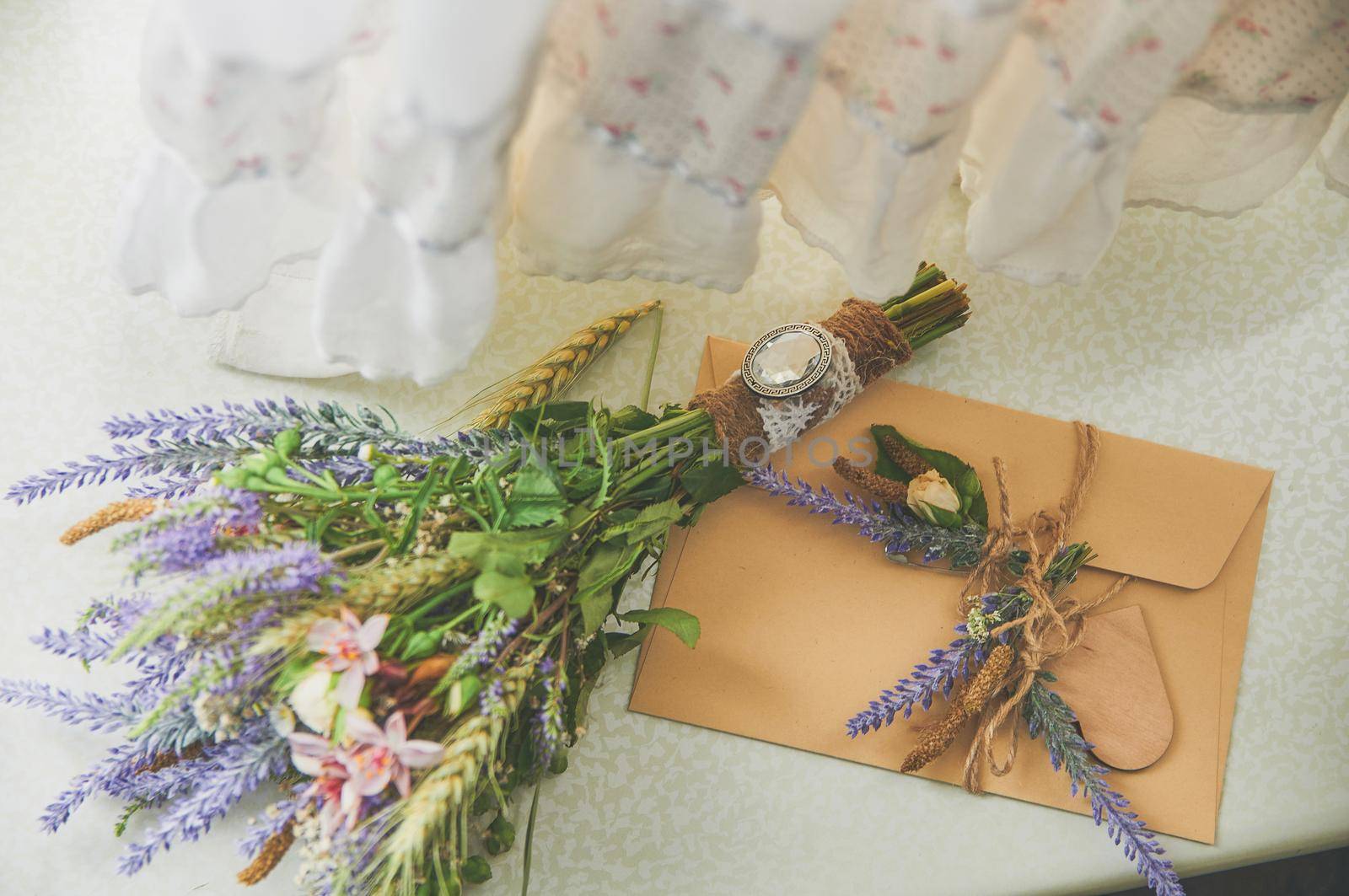 bridal bouquet of lavender in a boho style lies on the window near the handmade envelope, on top of the wedding dress