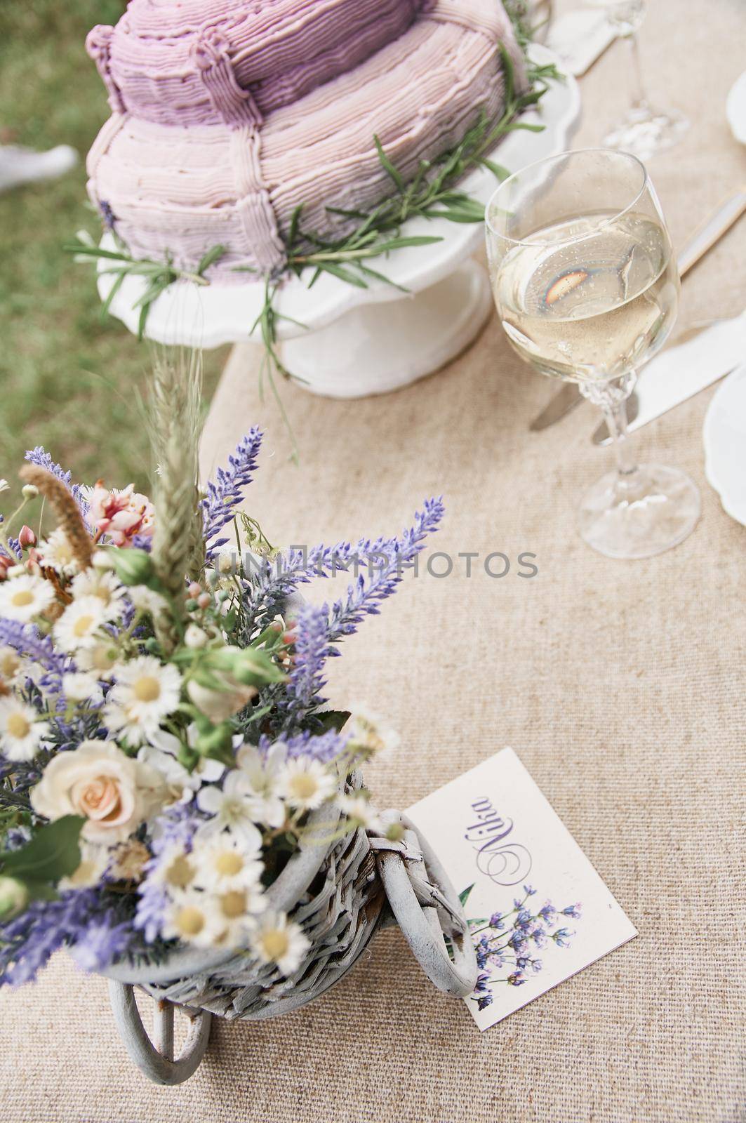 boho style wedding cake on a table covered with a linen tablecloth, with plates, glasses, knife fork and a bouquet of flowers