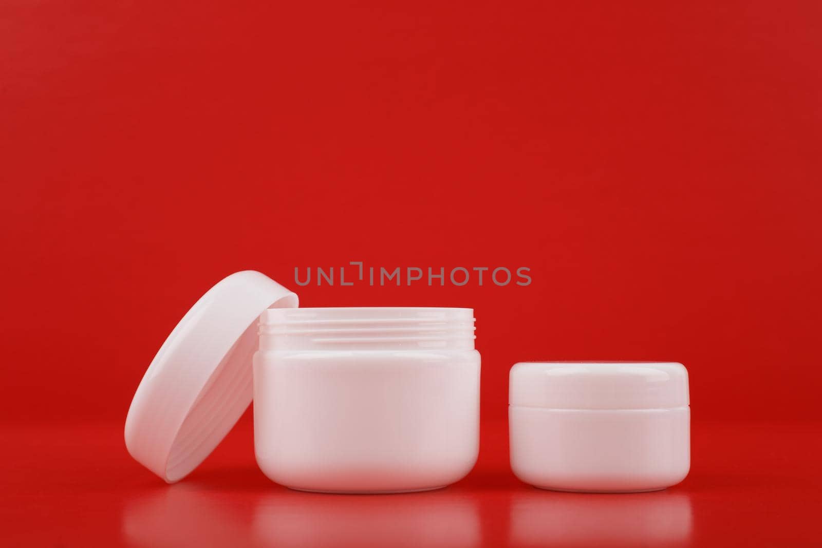 Two white cream jars against red background with copy space. Concept of luxury skin care or daily beauty treatment by Senorina_Irina