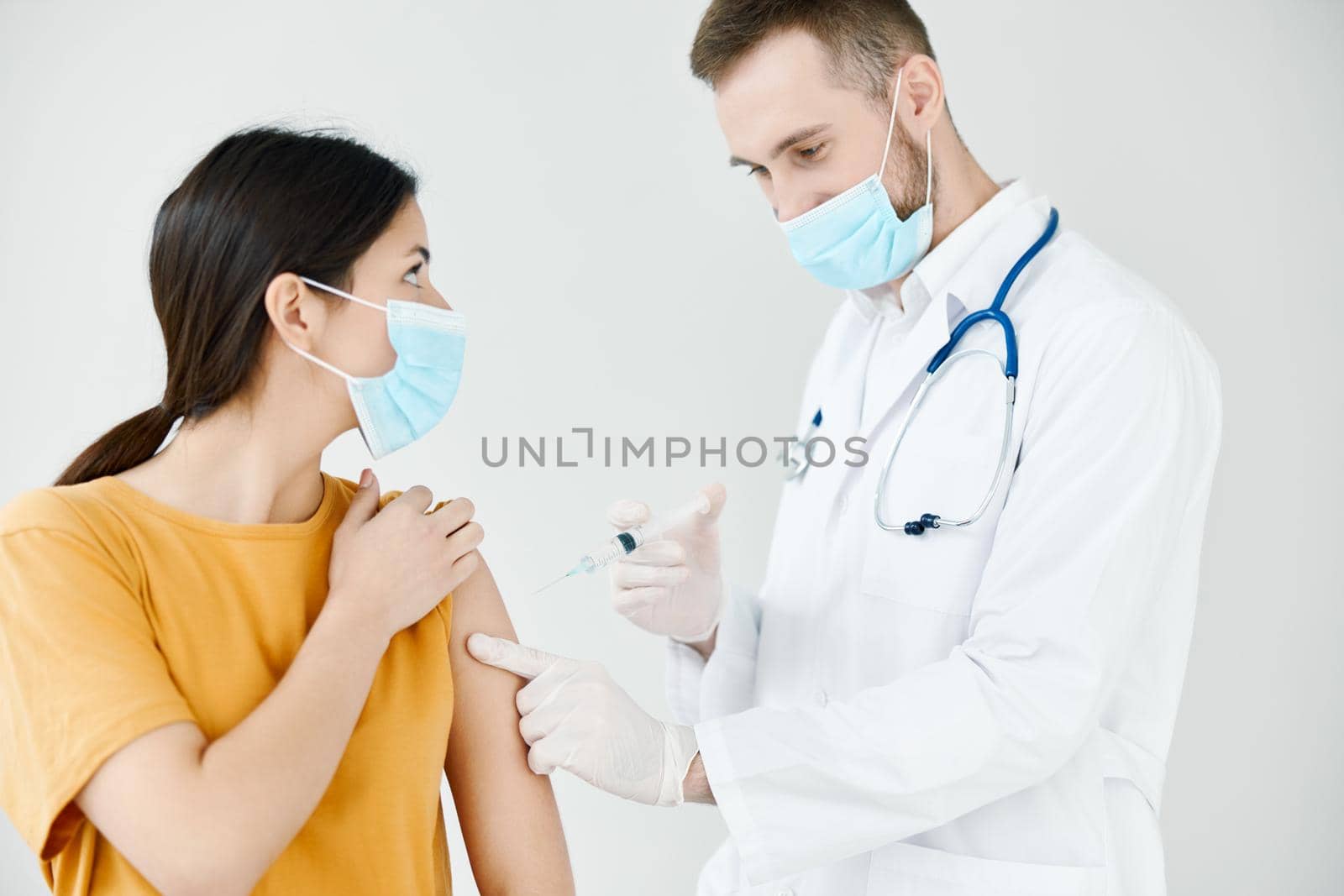 a patient in a medical mask looks at a doctor with a syringe in his hand vaccination infection by SHOTPRIME