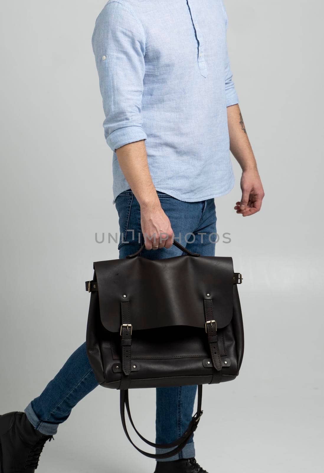Brown men's shoulder leather bag for a documents and laptop holds by man in a blue shirt and jeans with a white background. Satchel, mens leather handmade briefcase