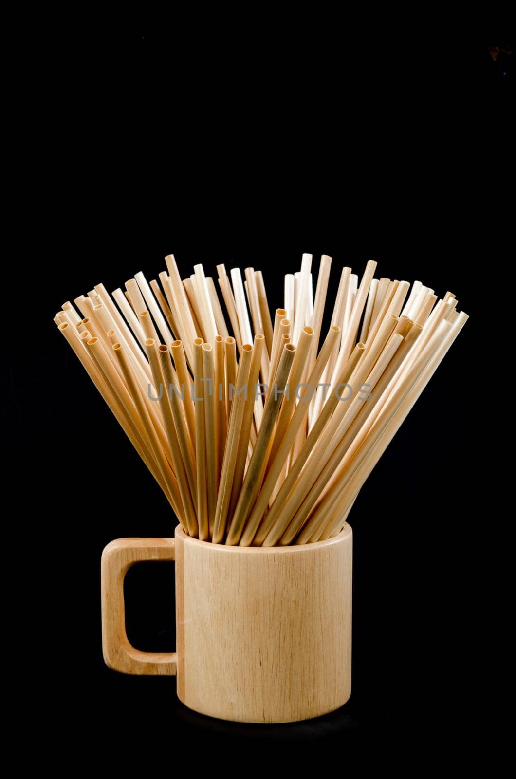 Wheat straw for drinking water in wooden glass on black background. Zero waste concept.
