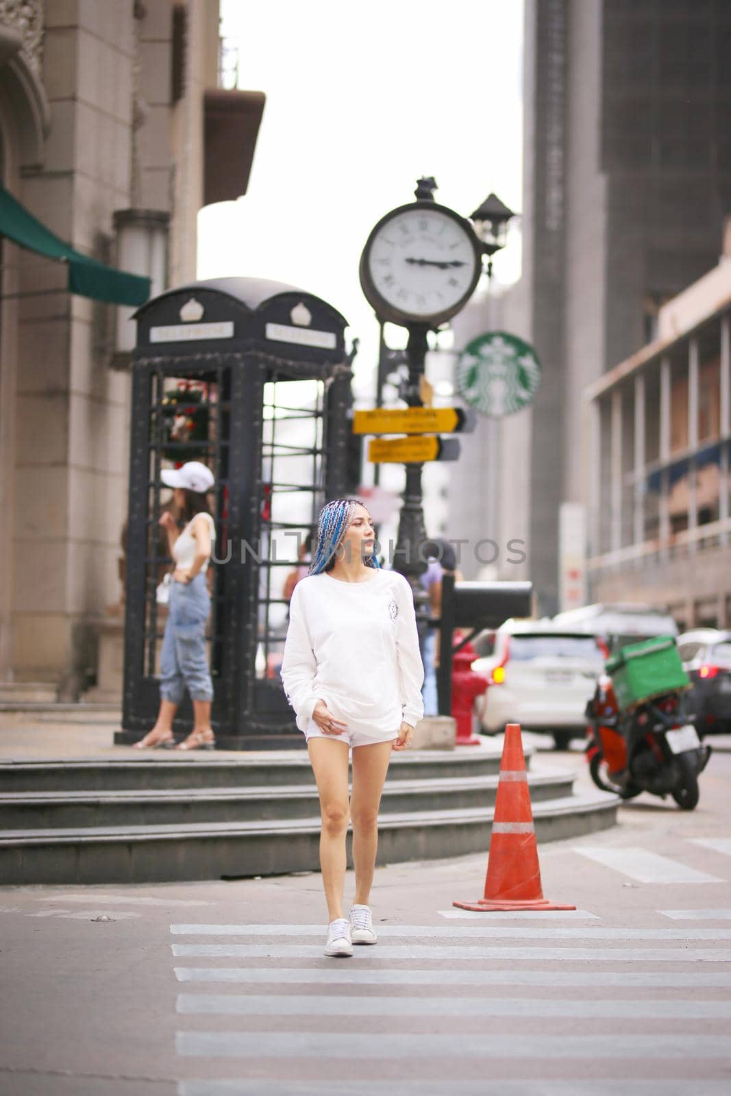 Happy stylish young hipster woman with long blue hair pink jacket, hat on the street in urban city.