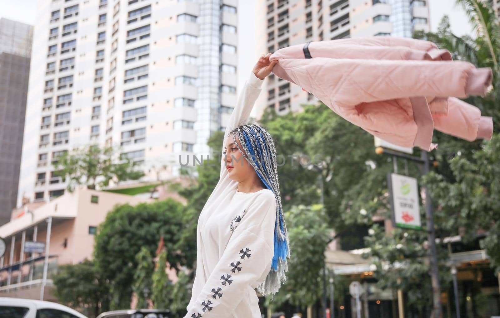 Happy stylish young hipster woman with long blue hair pink jacket, hat on the street in urban city. by chuanchai