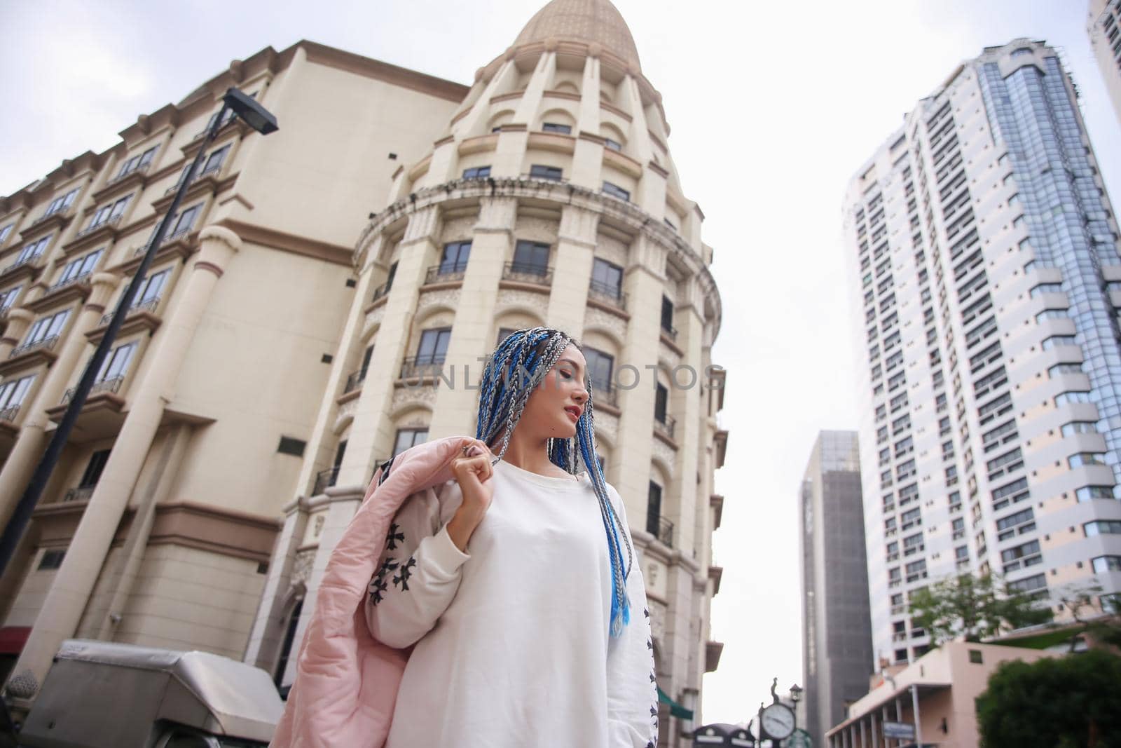 Happy stylish young hipster woman with long blue hair pink jacket, hat on the street in urban city. by chuanchai