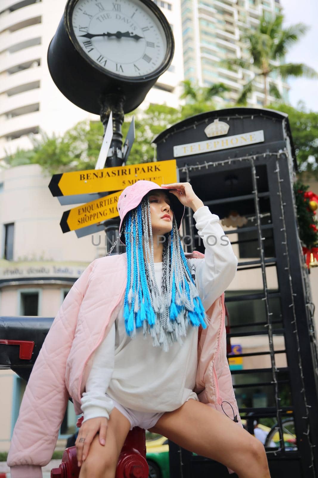 Happy stylish young hipster woman with long blue hair pink jacket, hat on the street in urban city.