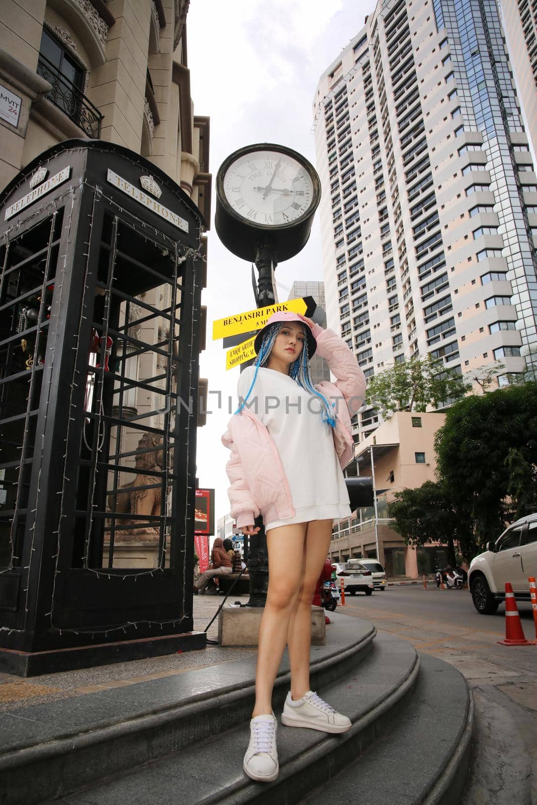 Happy stylish young hipster woman with long blue hair pink jacket, hat on the street in urban city.