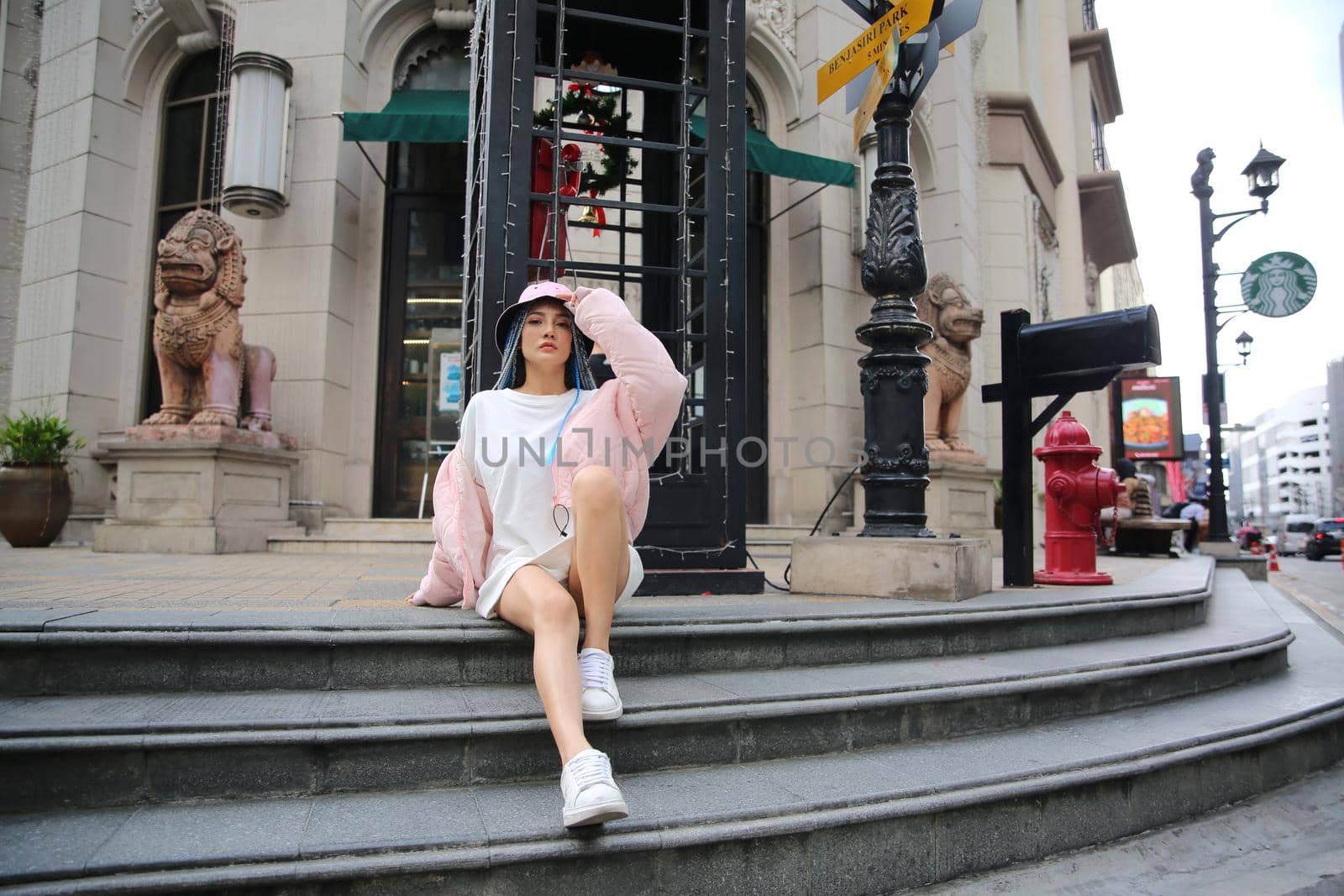 Happy stylish young hipster woman with long blue hair pink jacket, hat on the street in urban city. by chuanchai