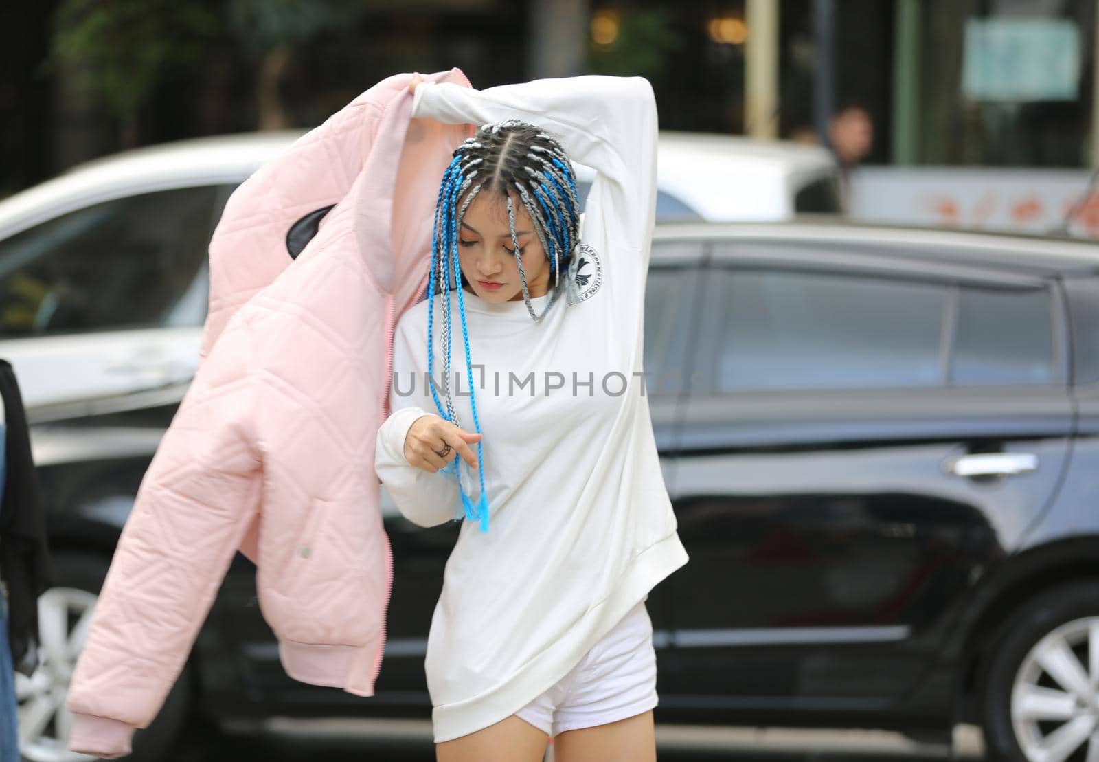 Happy stylish young hipster woman with long blue hair pink jacket, hat on the street in urban city. by chuanchai