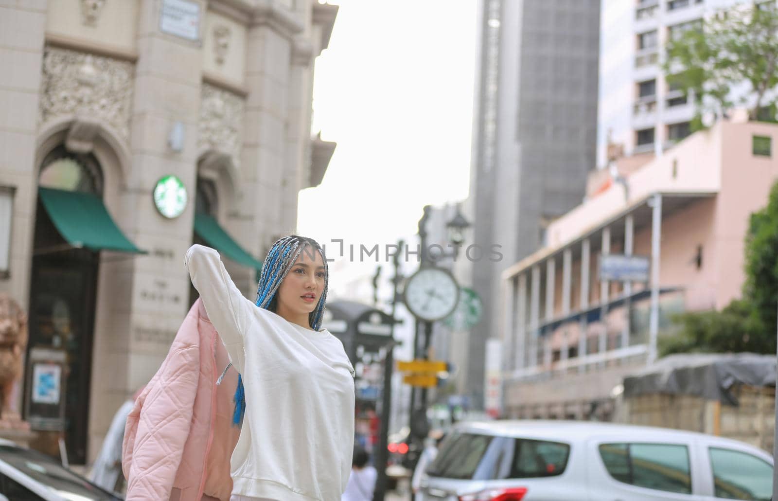 Happy stylish young hipster woman with long blue hair pink jacket, hat on the street in urban city. by chuanchai