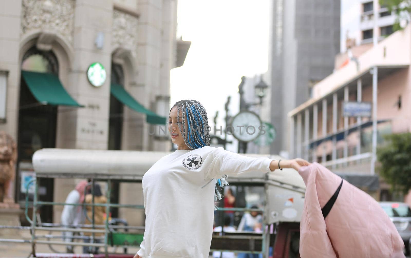 Happy stylish young hipster woman with long blue hair pink jacket, hat on the street in urban city. by chuanchai