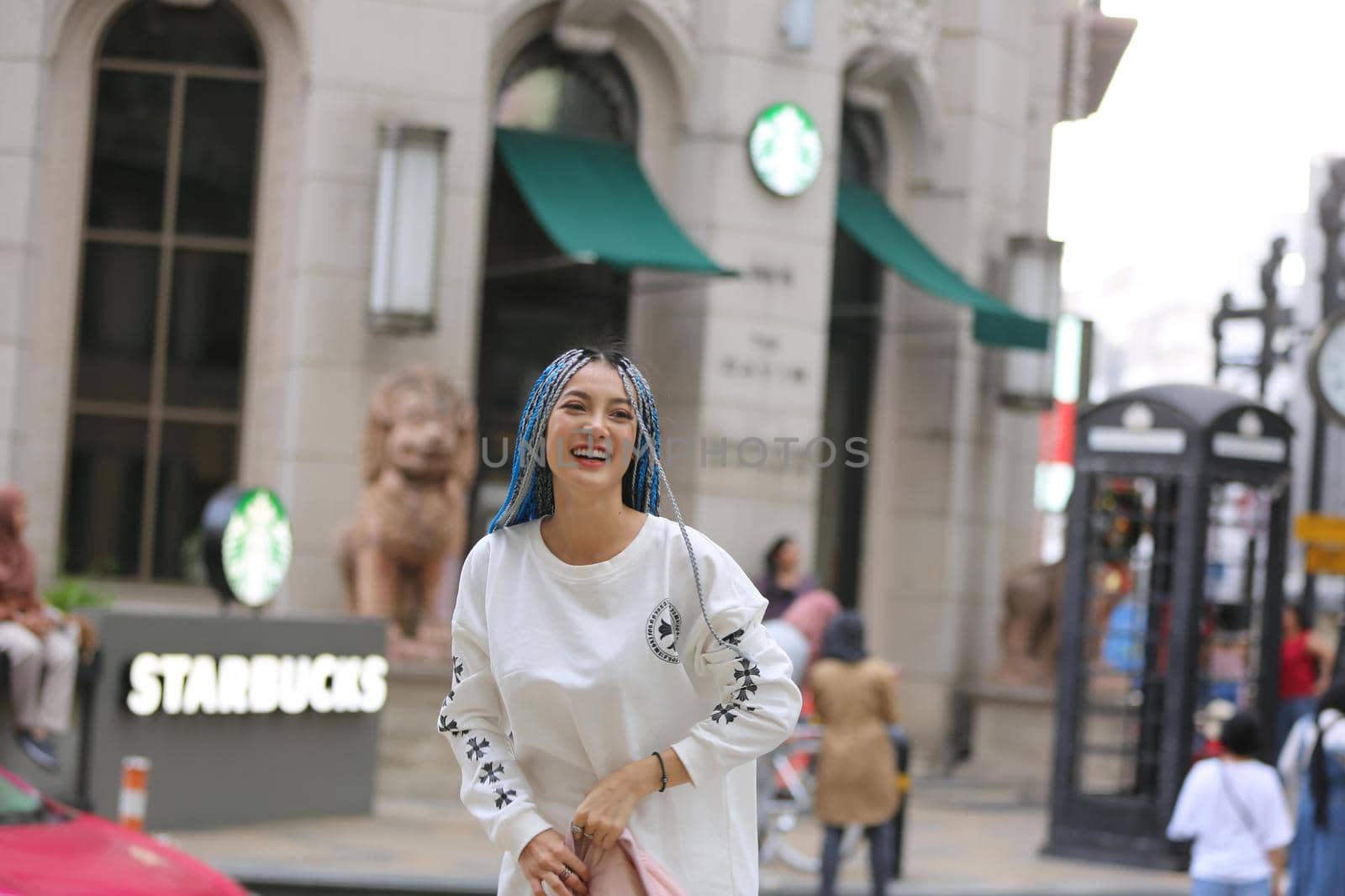 Happy stylish young hipster woman with long blue hair pink jacket, hat on the street in urban city. by chuanchai