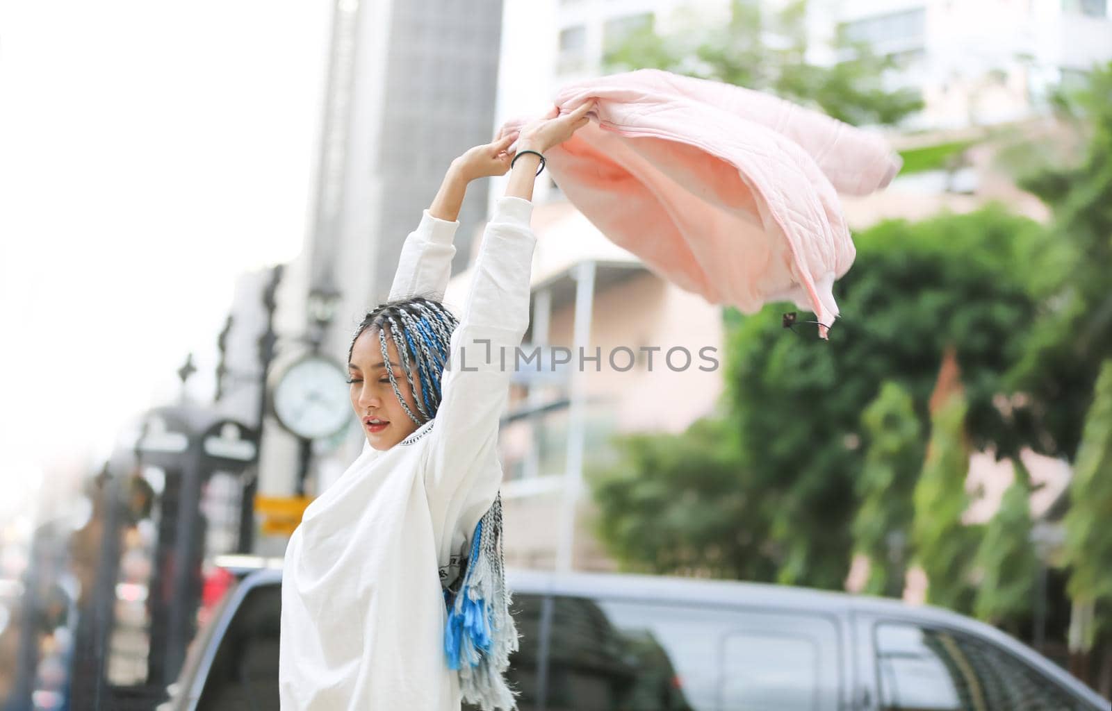 Happy stylish young hipster woman with long blue hair pink jacket, hat on the street in urban city.