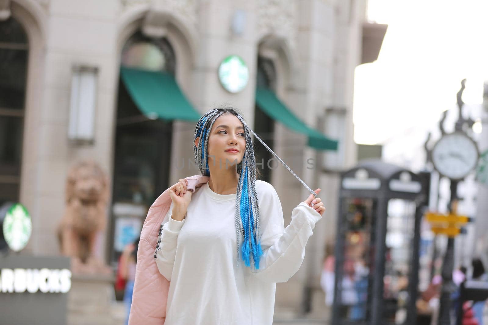 Happy stylish young hipster woman with long blue hair pink jacket, hat on the street in urban city.