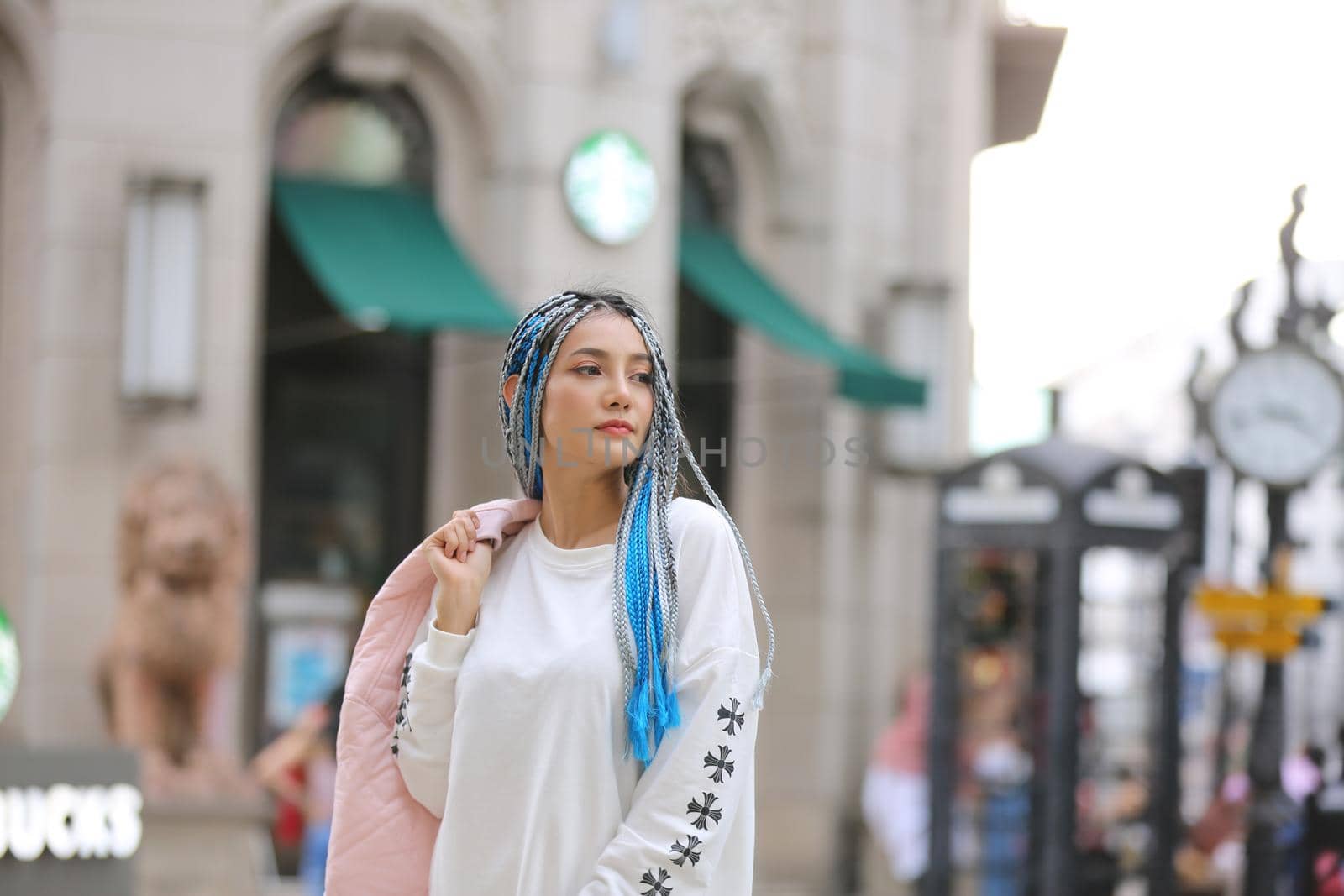 Happy stylish young hipster woman with long blue hair pink jacket, hat on the street in urban city. by chuanchai