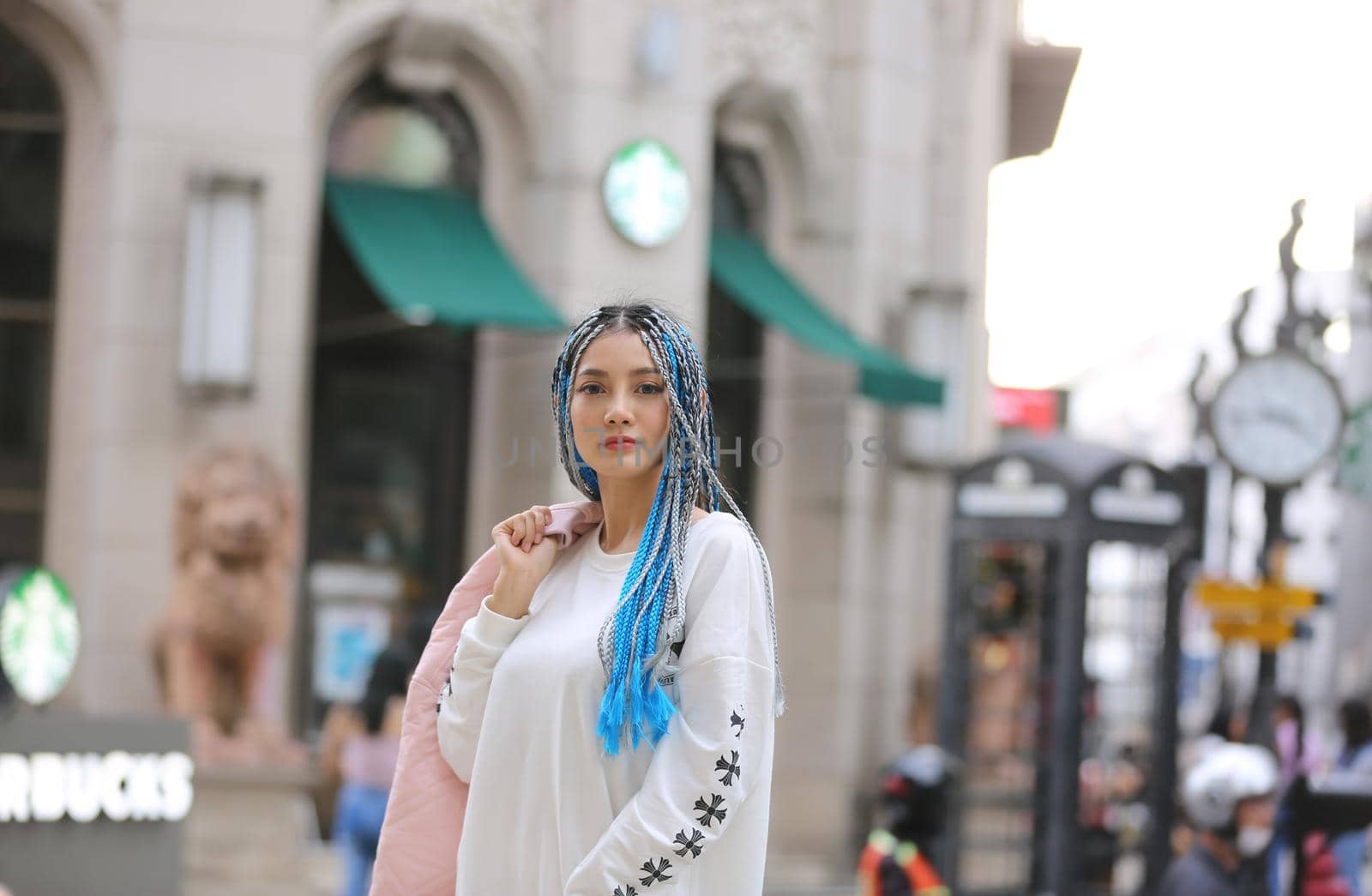 Happy stylish young hipster woman with long blue hair pink jacket, hat on the street in urban city. by chuanchai