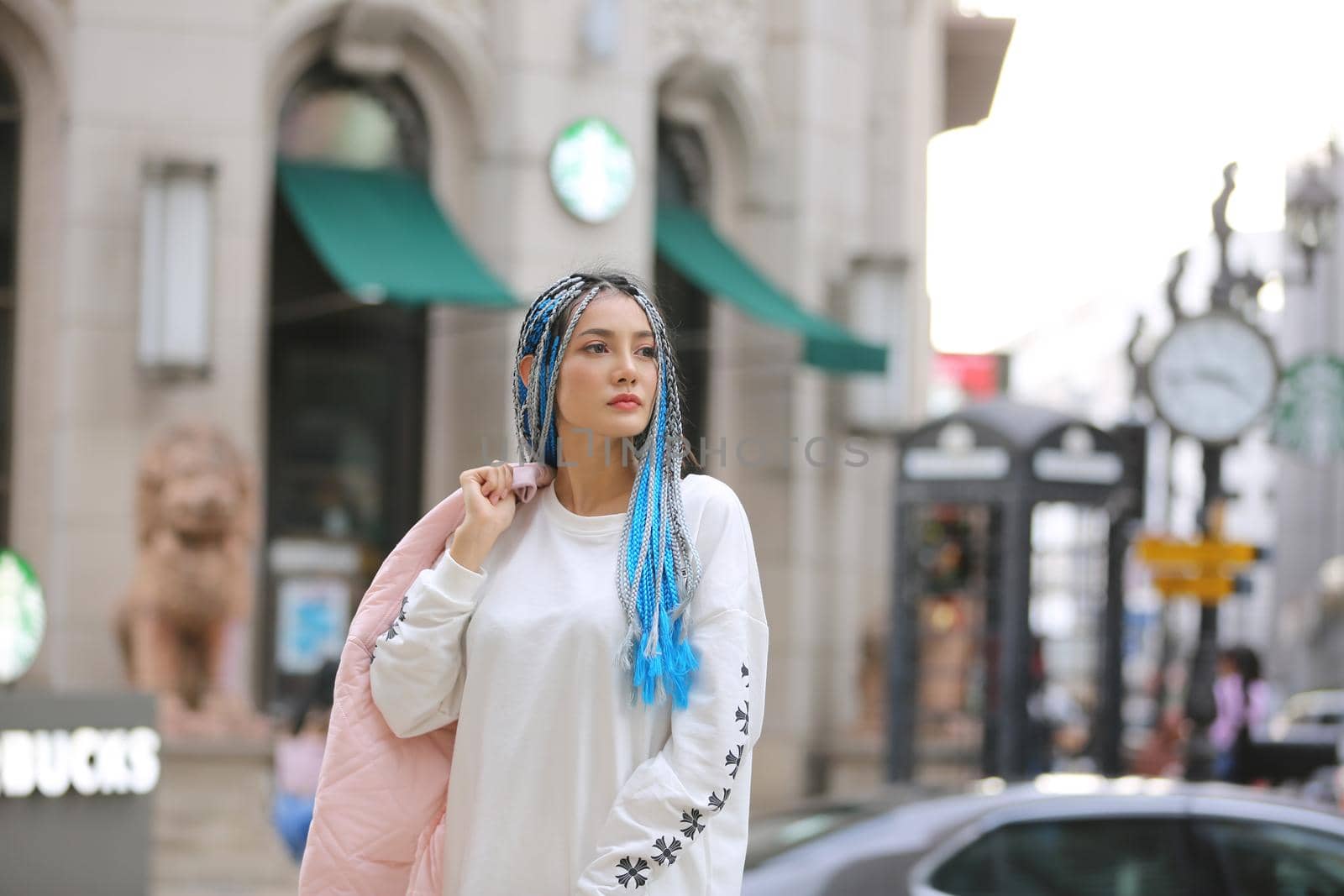 Happy stylish young hipster woman with long blue hair pink jacket, hat on the street in urban city. by chuanchai