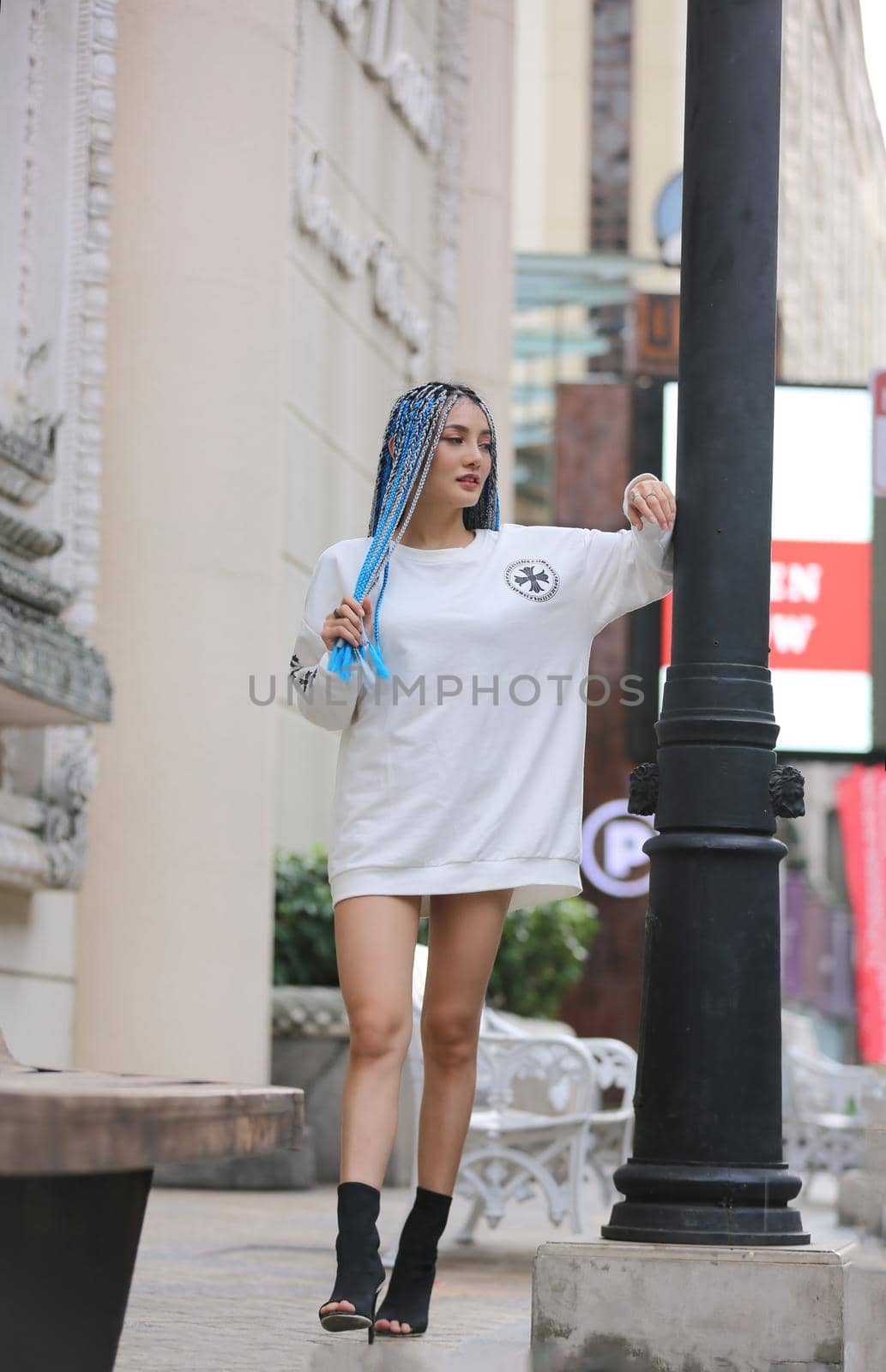 Happy stylish young hipster woman with long blue hair pink jacket, hat on the street in urban city.