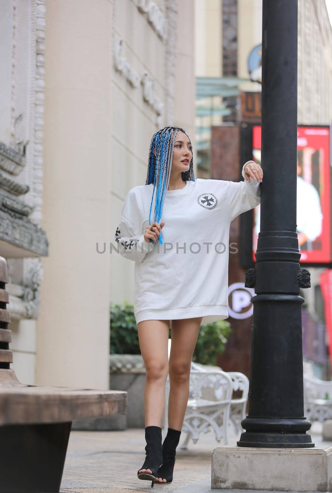Happy stylish young hipster woman with long blue hair pink jacket, hat on the street in urban city.