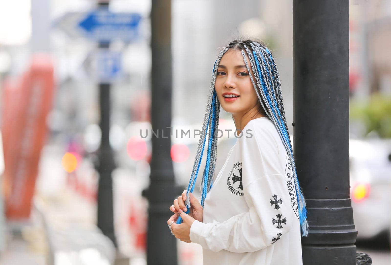 Happy stylish young hipster woman with long blue hair pink jacket, hat on the street in urban city.