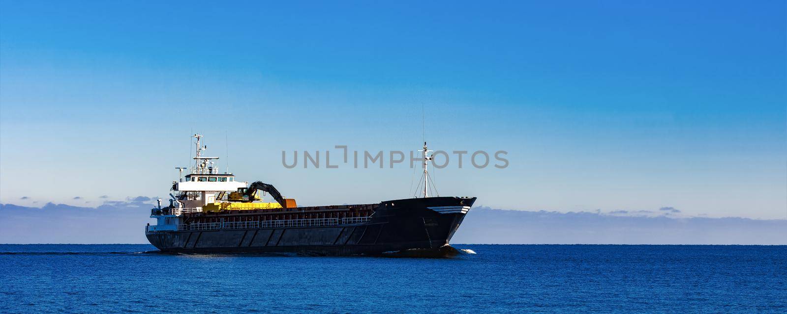 Black Sailing Bulk Carrier. Cargo Ship with Long Reach Excavator Moving in Still Water at Sunny Day by the Sea