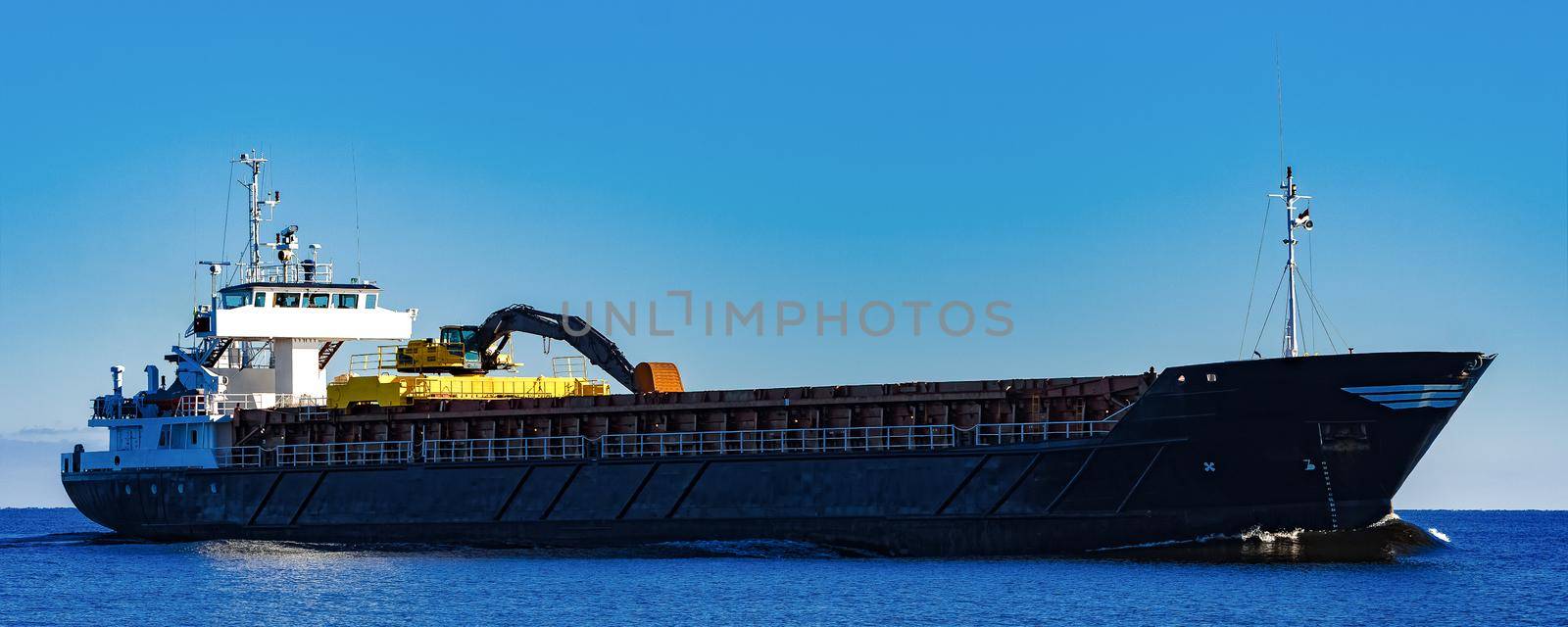 Black Sailing Bulk Carrier. Cargo Ship with Long Reach Excavator Moving in Still Water at Sunny Day by the Sea