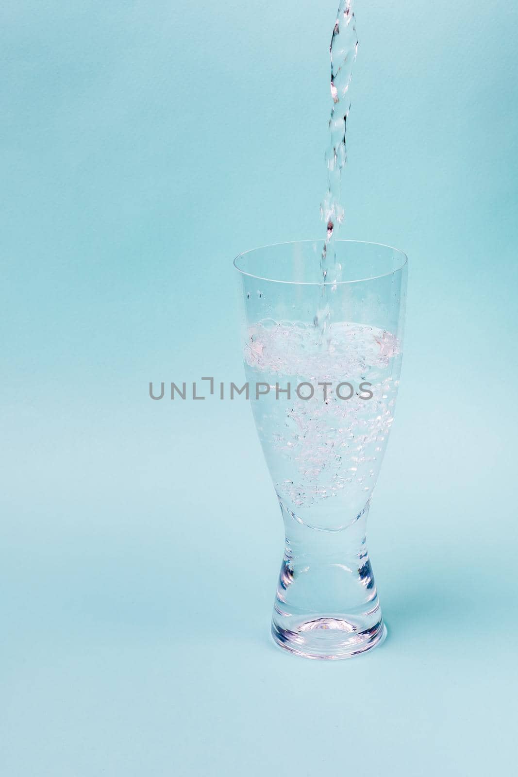 A jet of water fills transparent glass against a blue background. White bubbles rise.
