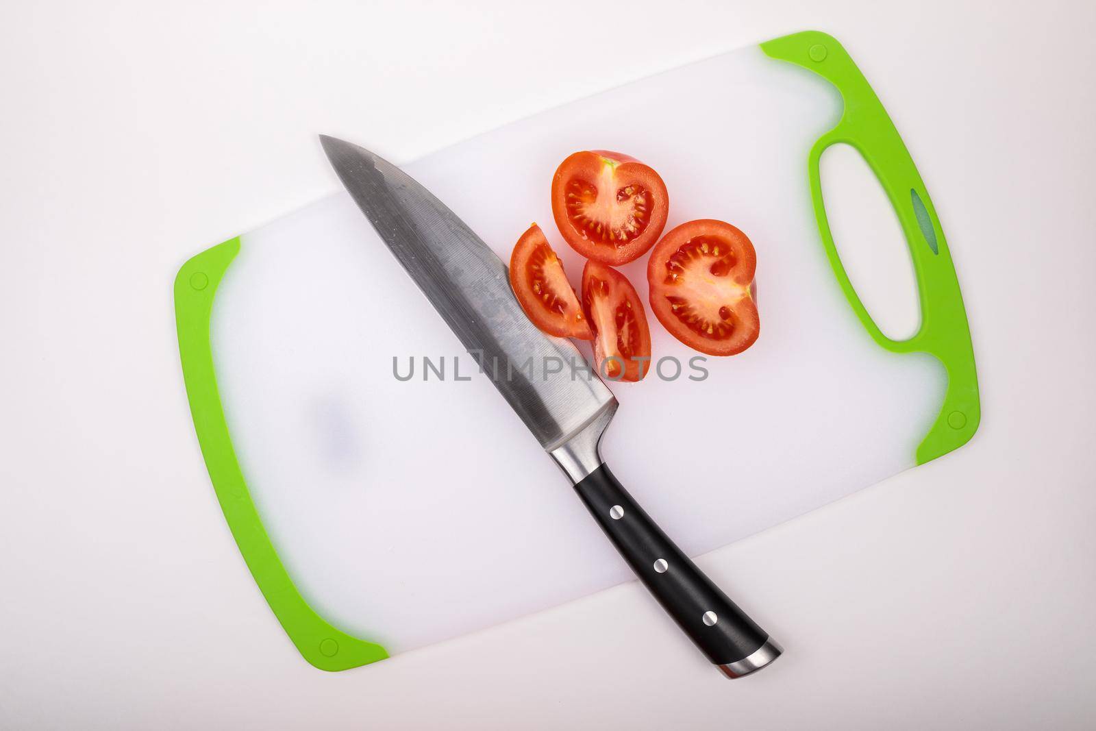 On a cutting board is a fresh red cut tomato and a large chef's knife. On an isolated white background.