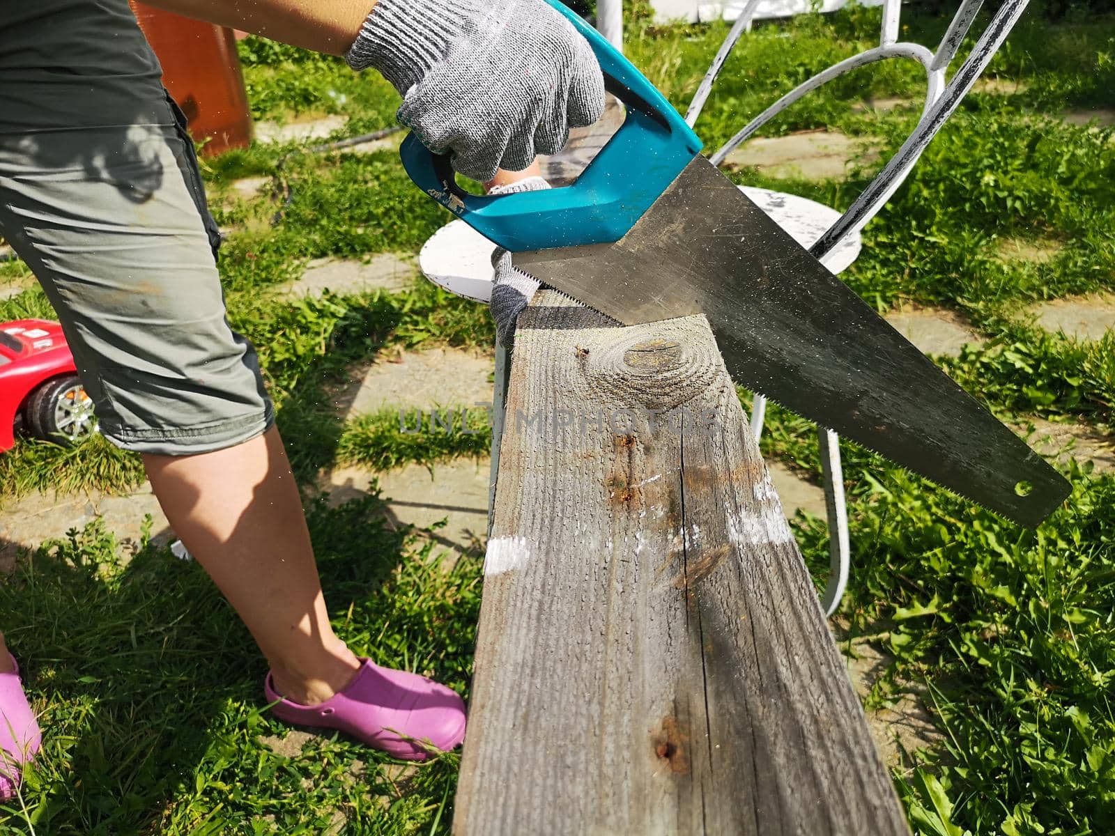 Farmer hand with saw cutting wooden boards in the garden.