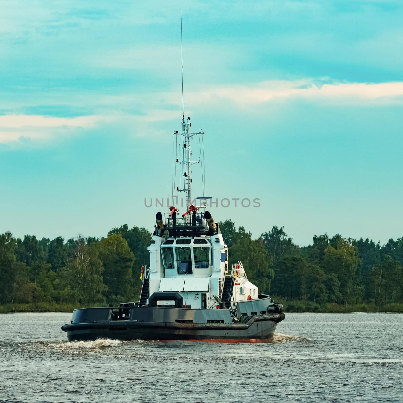 Black tug ship moving to the cargo terminal. Industrial service