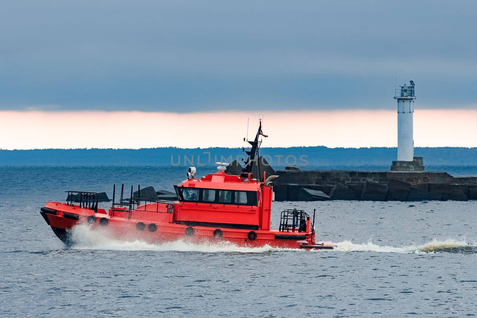 Red pilot ship moving at speed past the lighthouse in Riga