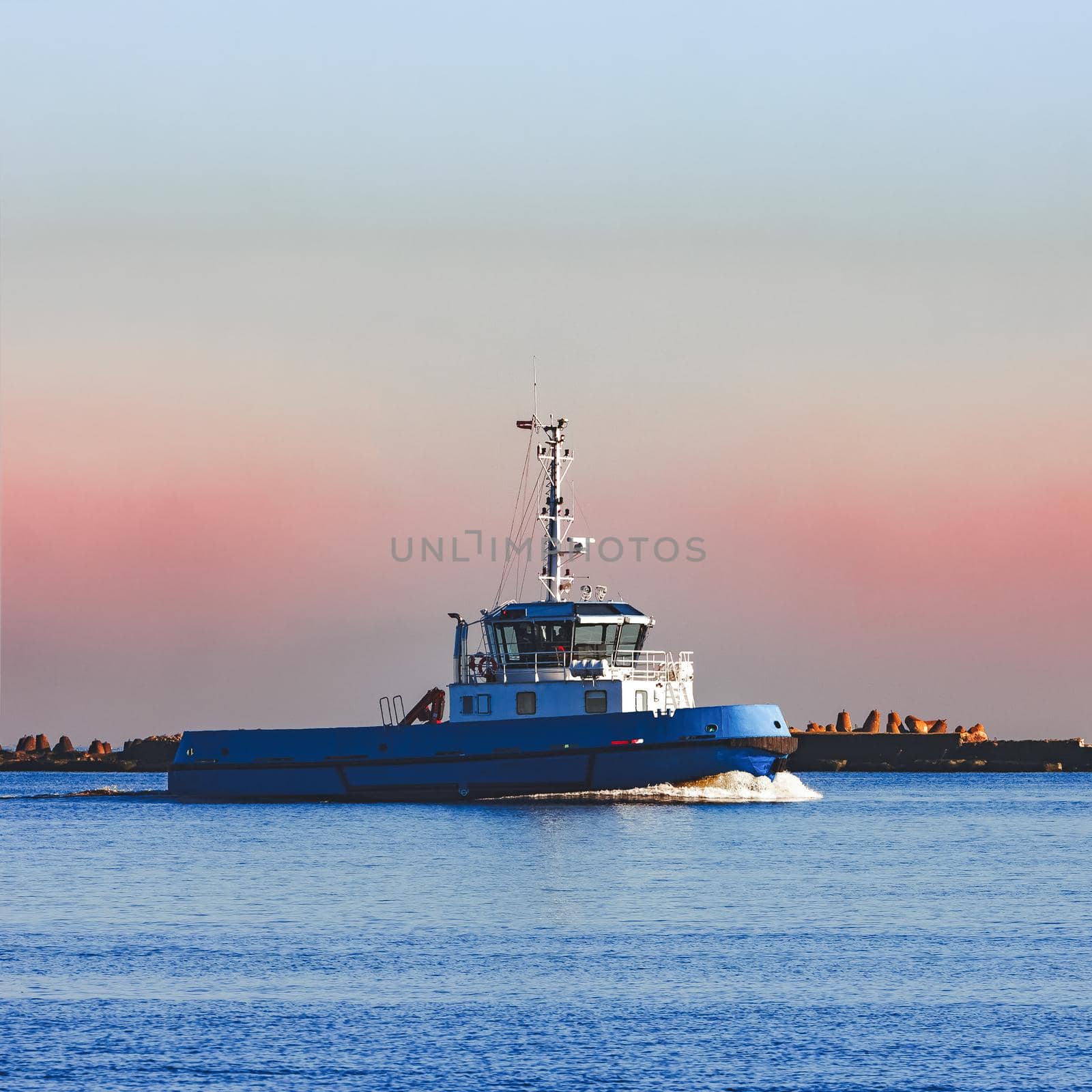 Blue small tug ship sailing past the breakwater dam in morning