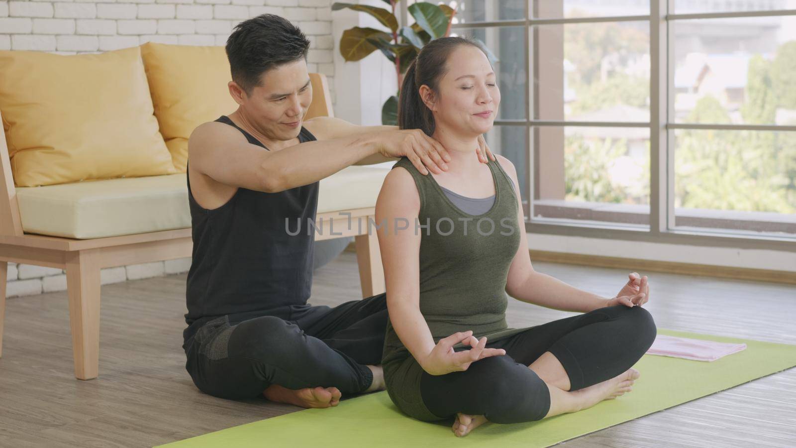 Happy Asian beautiful lifestyle family couple, woman doing YOGA sitting meditating on lotus pose workout at home and the man massage shoulder for relax. sport healthy concept