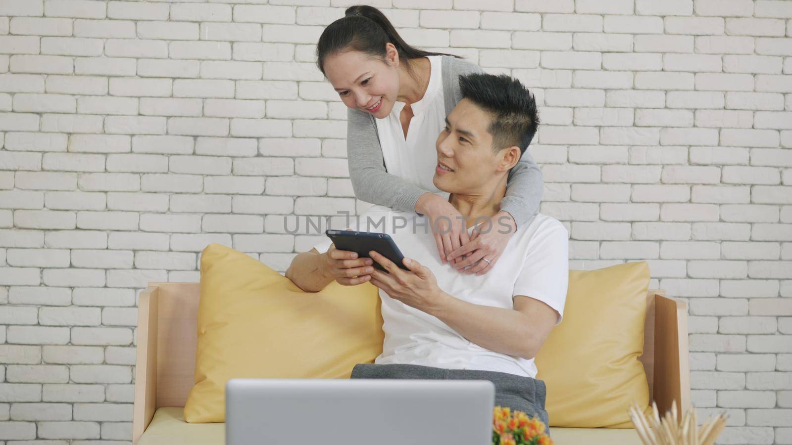 Asian family couple husband and wife work and using digital tablet. Cheerful loving couple smile shopping something online and watching social media together from home in living room,