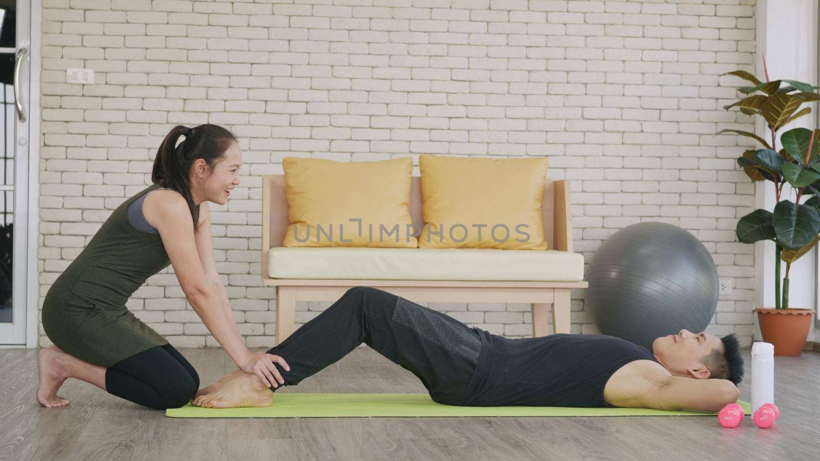 Happy Asian family couple husband and wife healthy trainer workout home in the living room. Fit man lifestyle doing sit up fitness exercise at home on floor with girlfriend support helping boyfriend