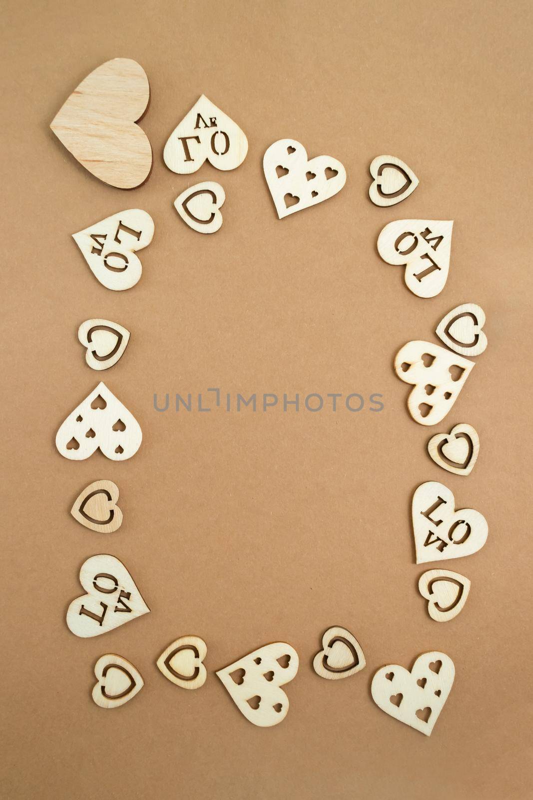 Wooden hearts on a pastel craft paper background in the form of a frame. Abstract background with wood cut shapes. Sainte Valentine. Copy space.