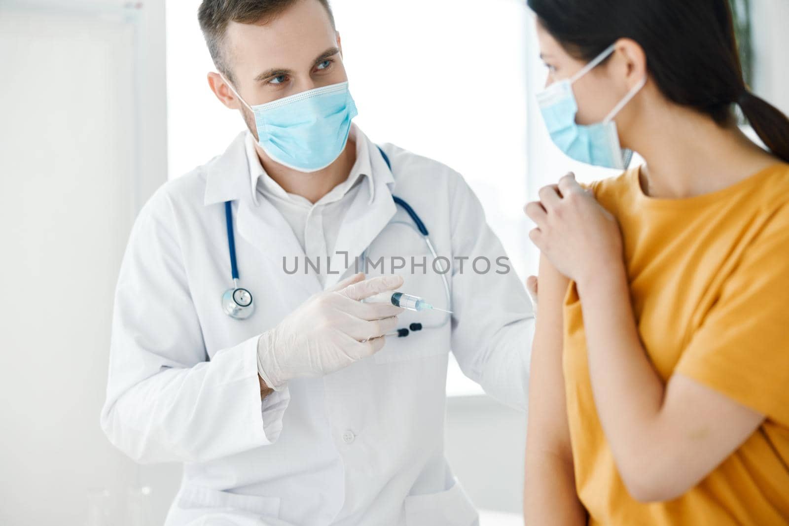 a laboratory assistant in a medical gown holds syringes in his hand and a patient covid vaccination by SHOTPRIME