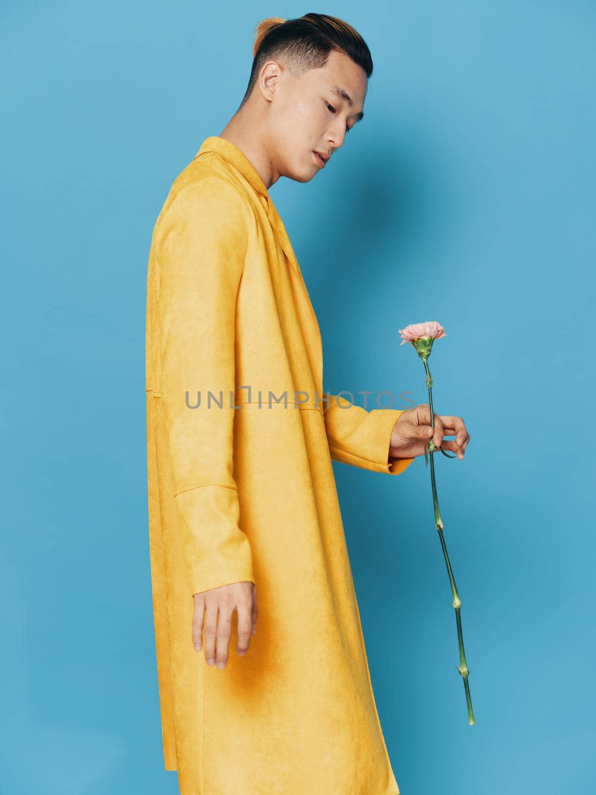 Side view of sexy Asian man in yellow coat on blue background Copy Space by SHOTPRIME