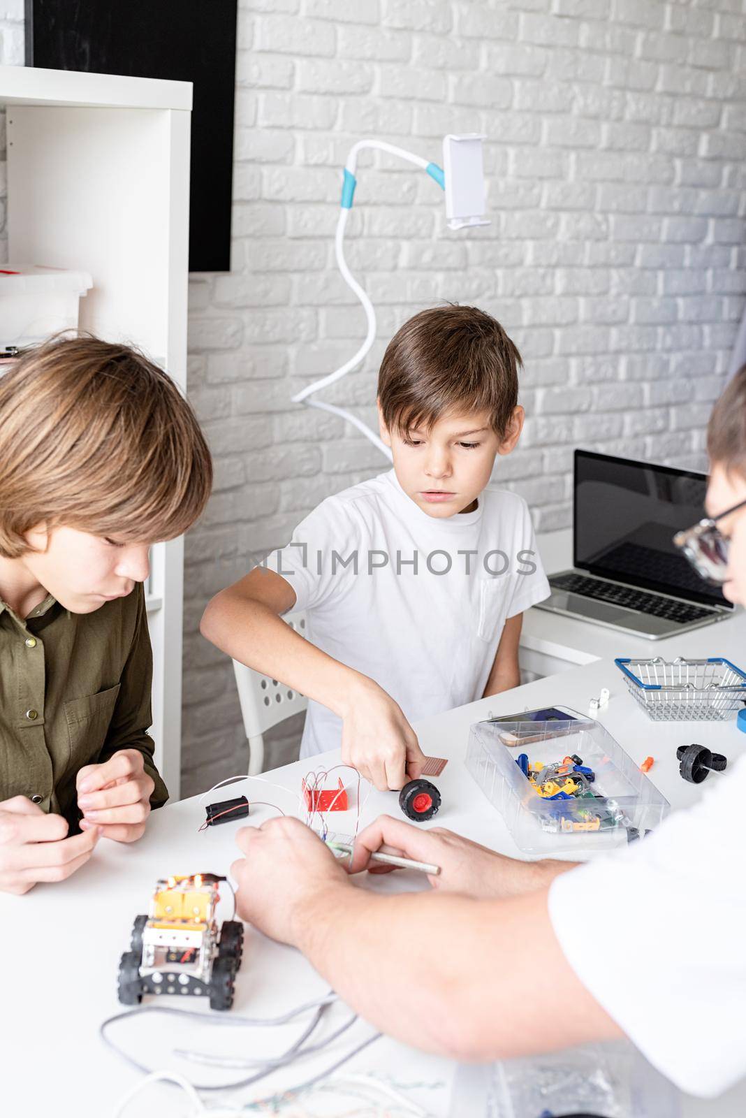 Young boys and teacher having fun constructing robot cars together at the workshop
