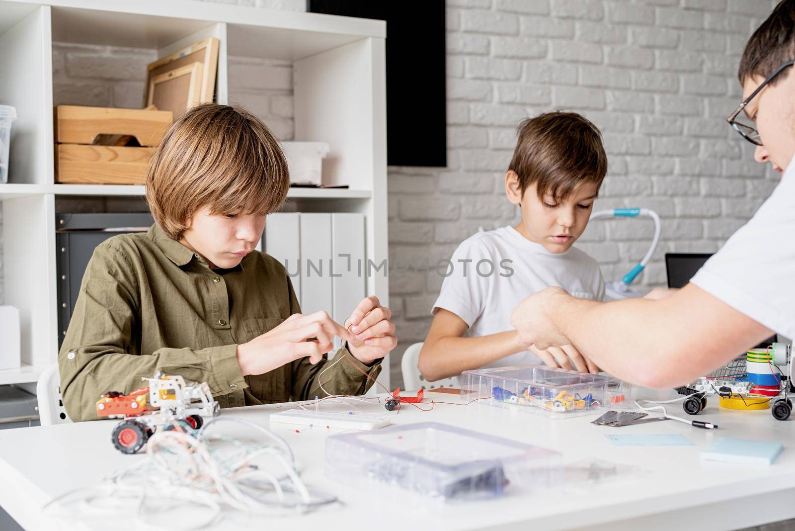Young boys and teacher having fun constructing robot cars together at the workshop