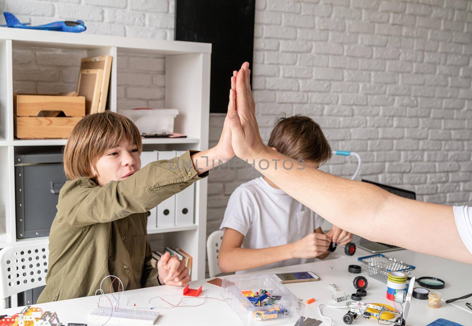 Young boys and teacher having fun constructing robot cars at the workshop giving each other high five