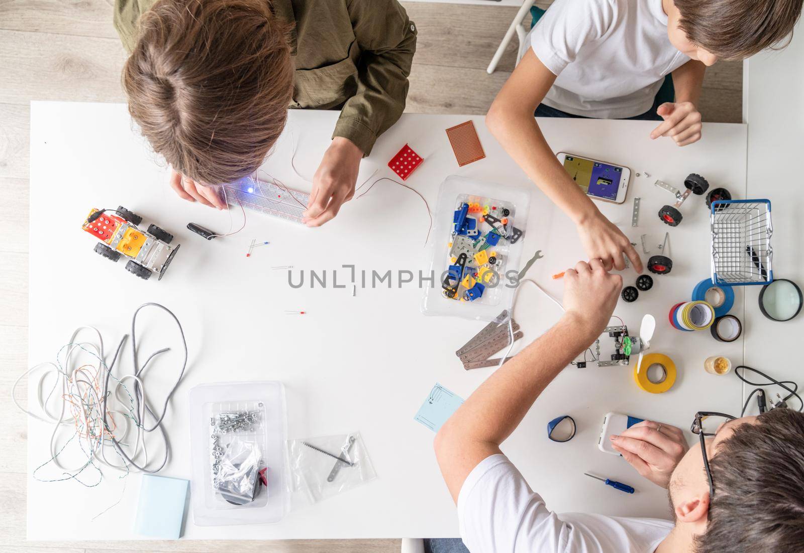 Young boys and teacher having fun constructing robot cars at the workshop, top view by Desperada