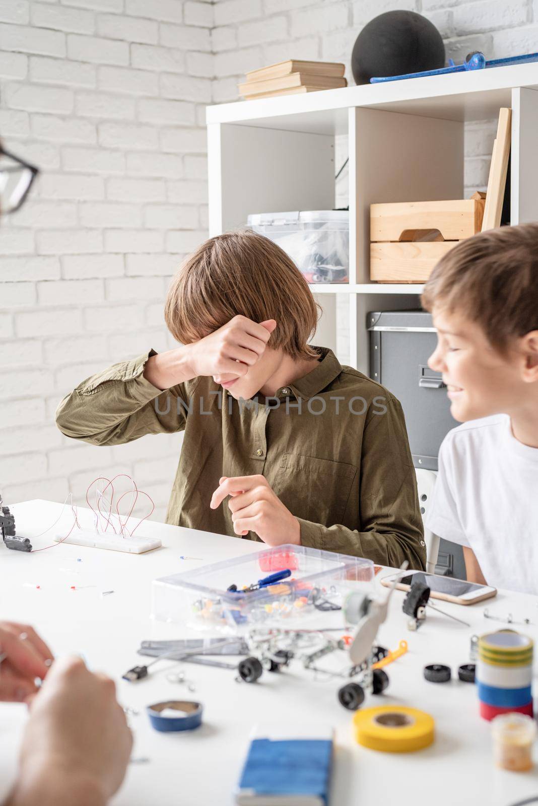 Tired boy working on a science project wiping his face by Desperada