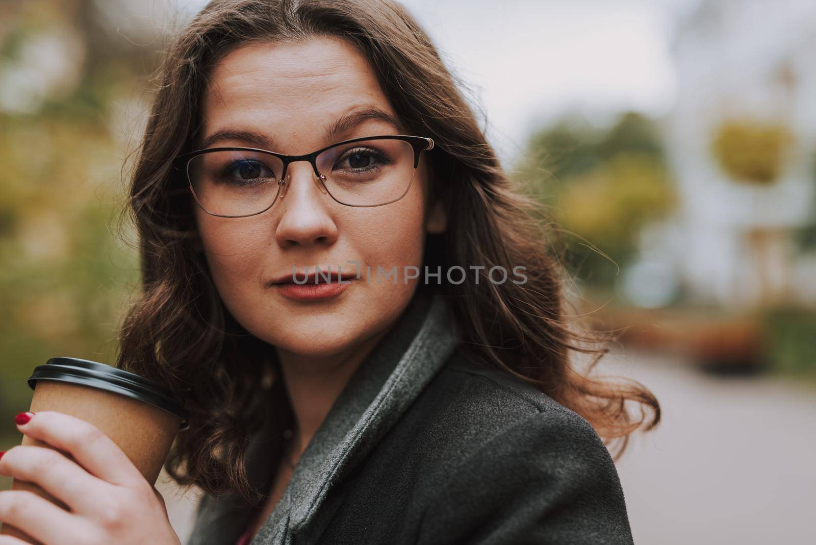 Portrait of attractive bespectacled young woman in the street holding a cup of coffee to go