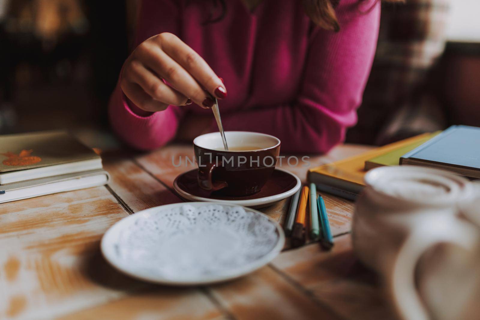 Woman holding a teaspoon in a cup with tea by monakoartstudio