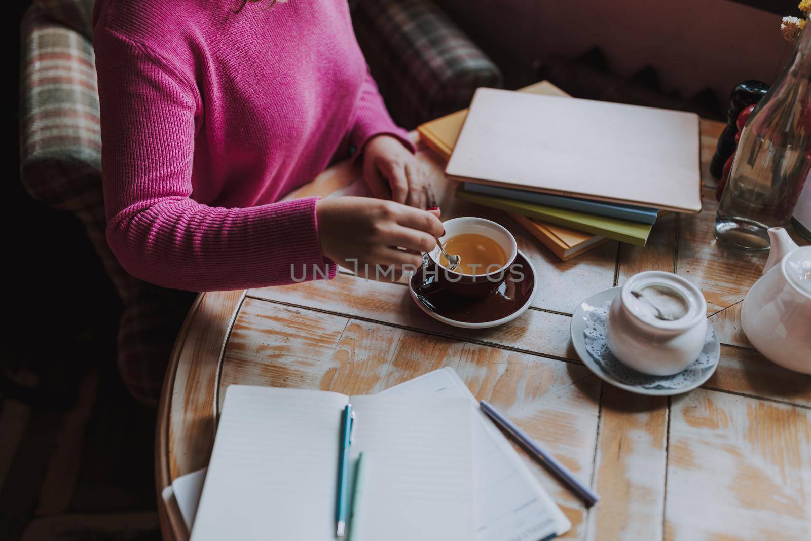 Top view of young lady studying in cafeteria and enjoying hot drink while stirring tea with a teaspoon