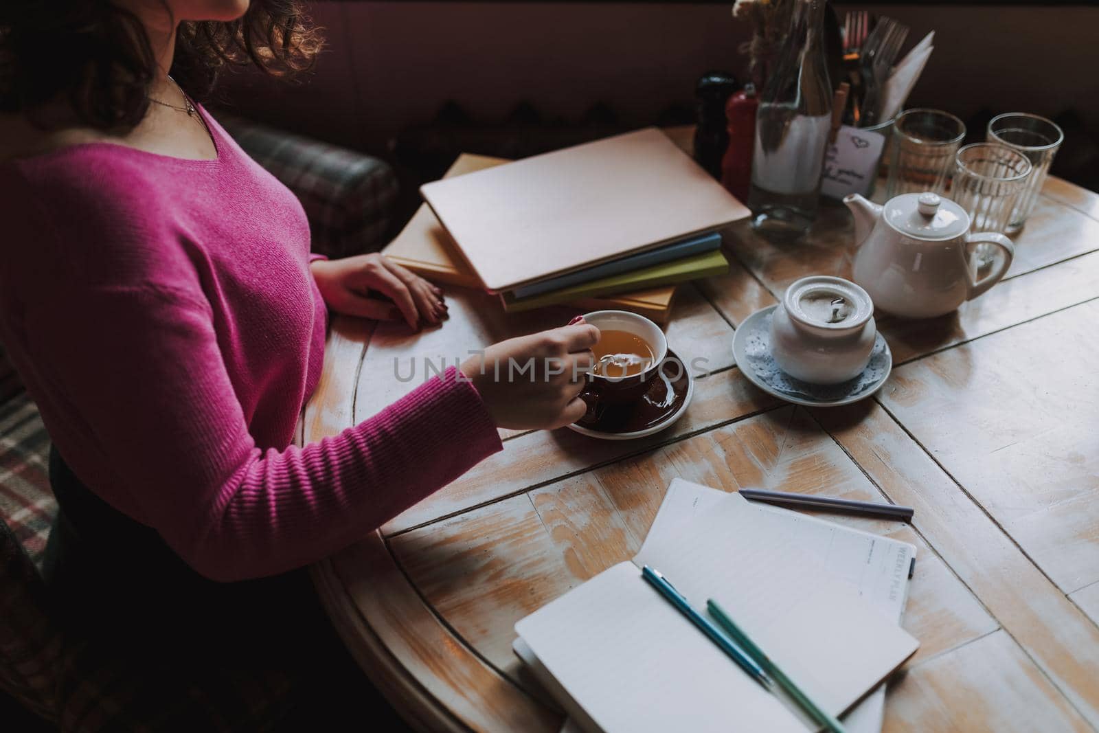 Top view of female student stirring tea with a teaspoon while sitting in cafe during lunch