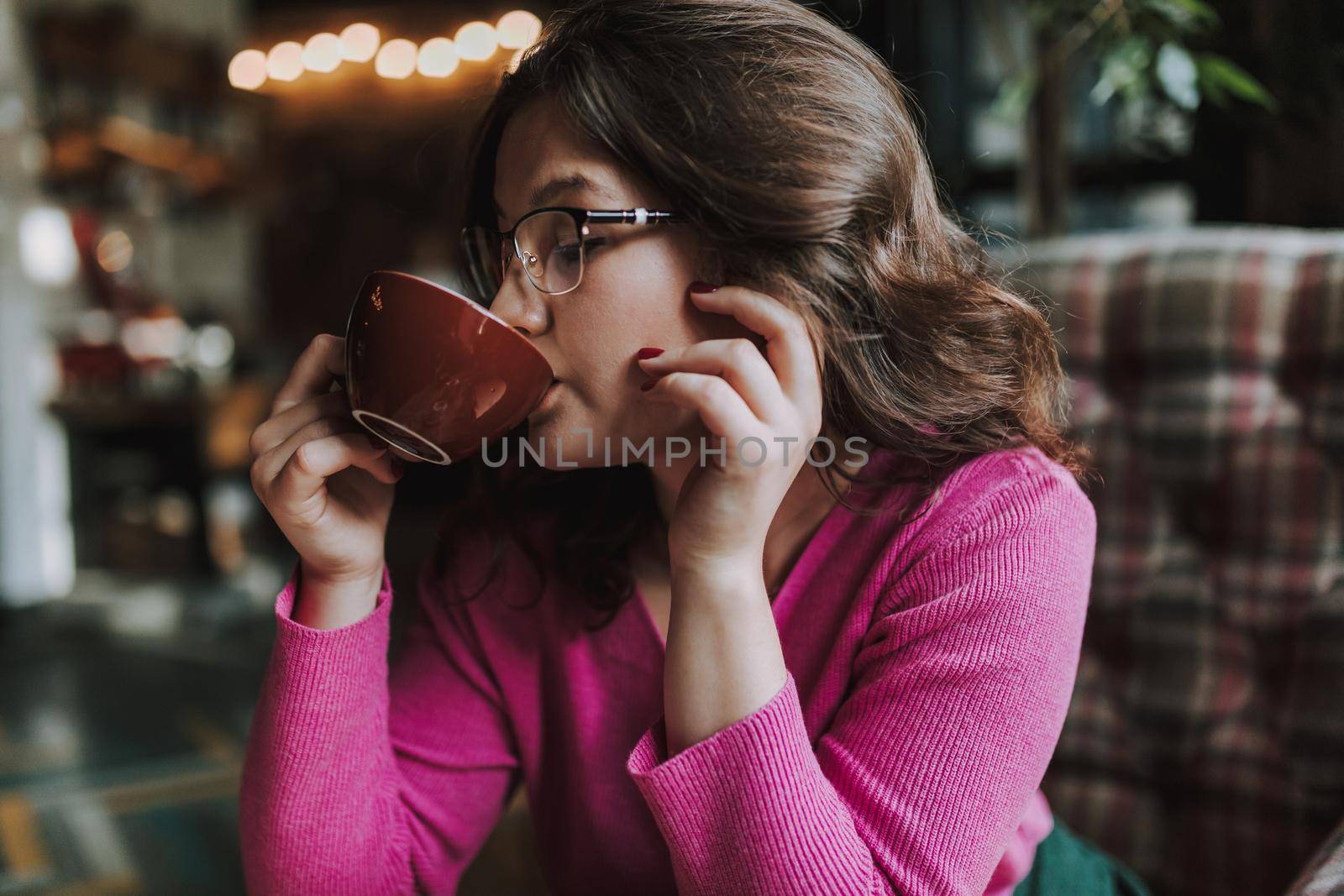 Portrait of pretty lady wearing glasses and sitting in coffee shop with hot drink