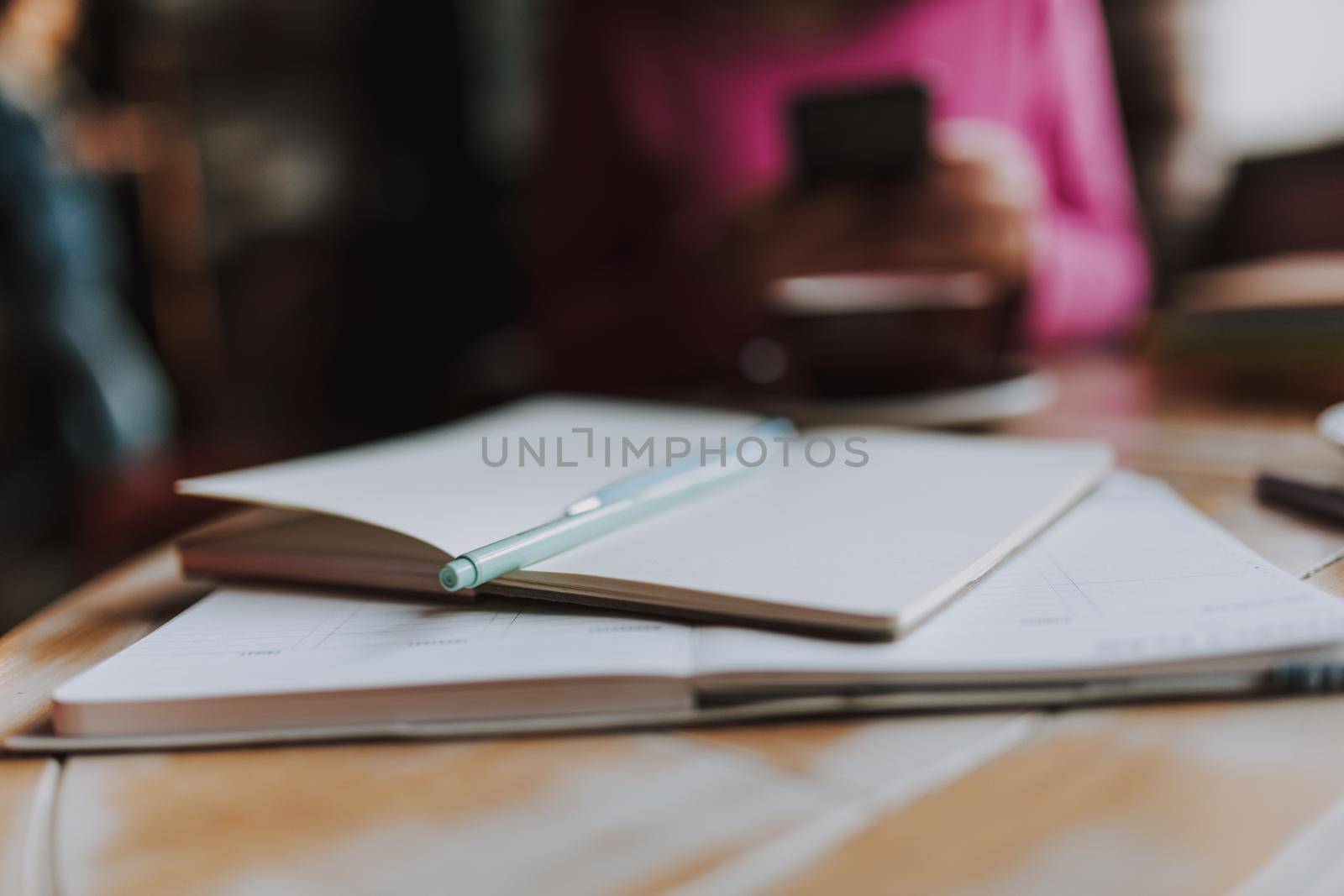Close up of notebooks with pen on the table with woman holding smartphone on the background